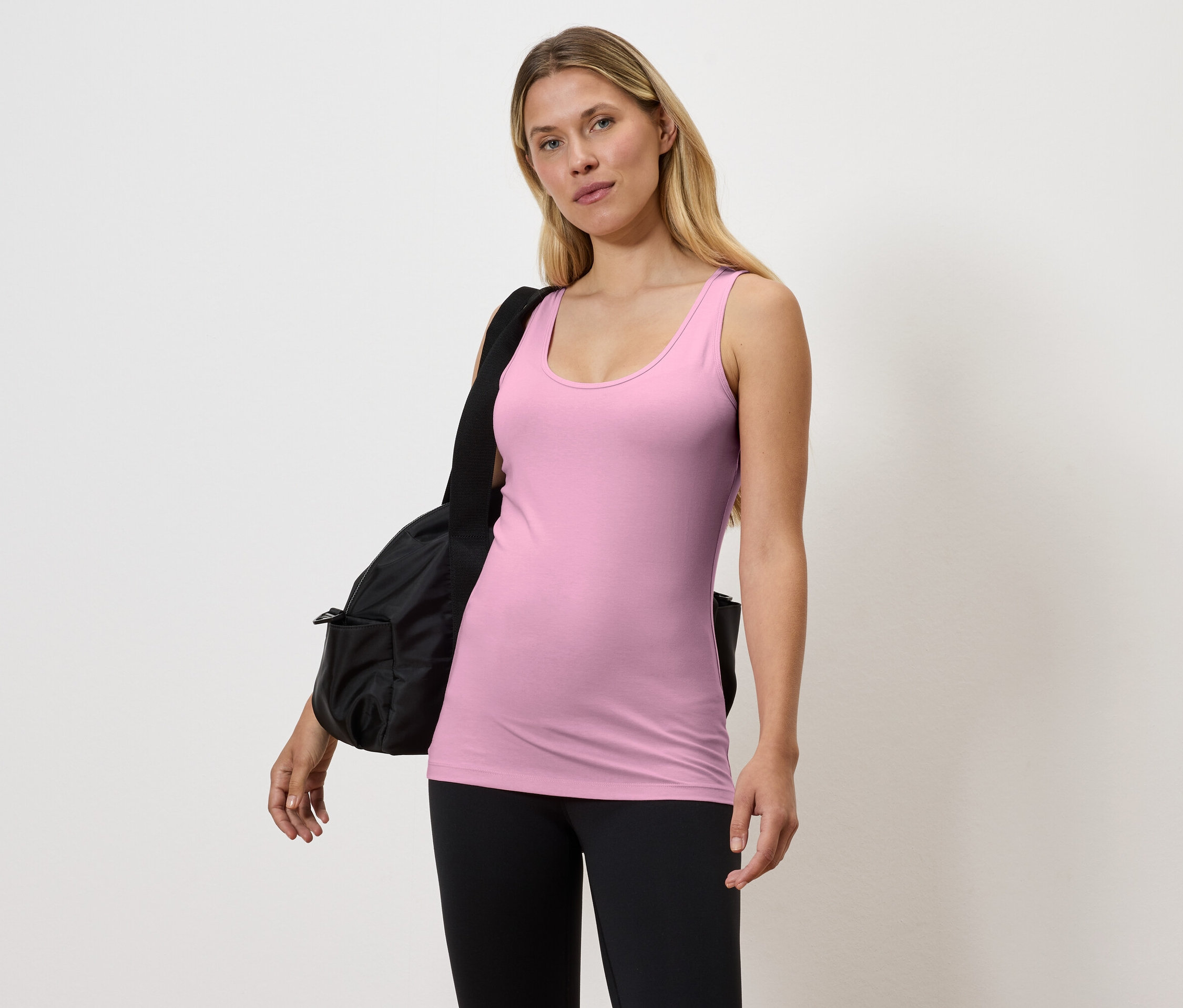 Frau in rosa Tanktop und schwarzen Leggings mit schwarzer Tasche über der Schulter.
