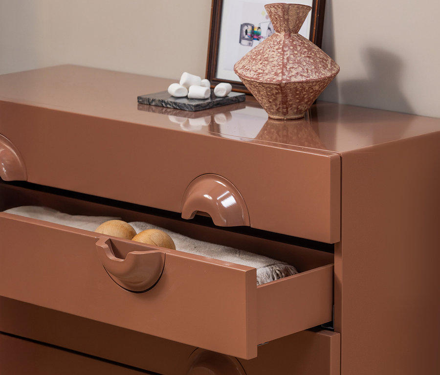 Detailaufnahme einer WOOOD »Merge« Kommode in Kupferbraun mit teilweise geöffneter Schublade, darin helle Textilien und zwei Holzkugeln.