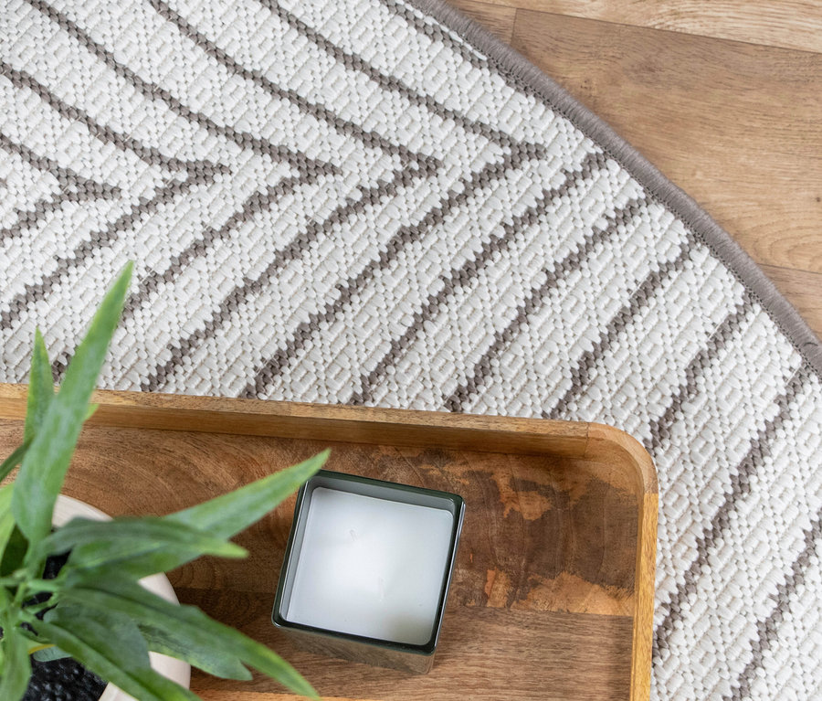 Nahaufnahme eines Dekotabletts mit einer Kerze und einer Pflanze vor einem gemusterten Teppich.