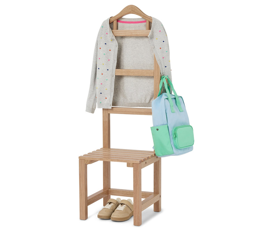 Ein grauer Cardigan mit bunten Punkten hängt auf einem Stuhl mit einer hellblauen und grünen Tasche. Unter dem Stuhl stehen beigefarbene Schuhe.