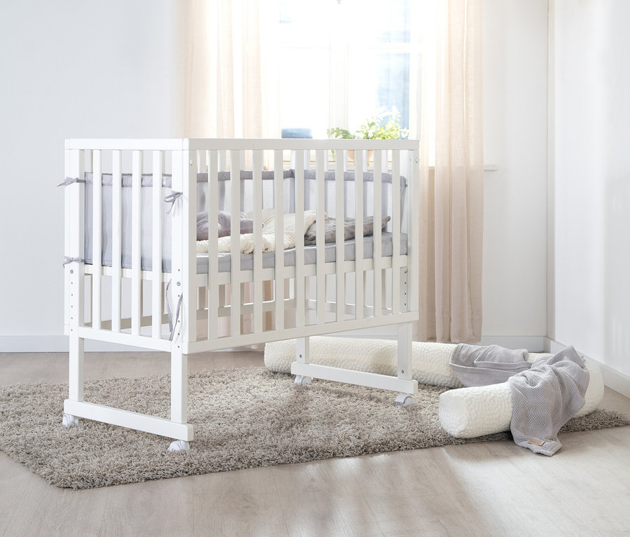 Weißes roba 3-in-1-Stuben-Beistellbett mit grauer Polsterung steht auf einem Teppich.