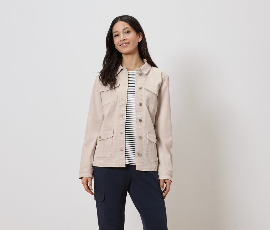 Frau trägt eine beige Jacke über einem gestreiften Hemd und marineblaue Hosen.