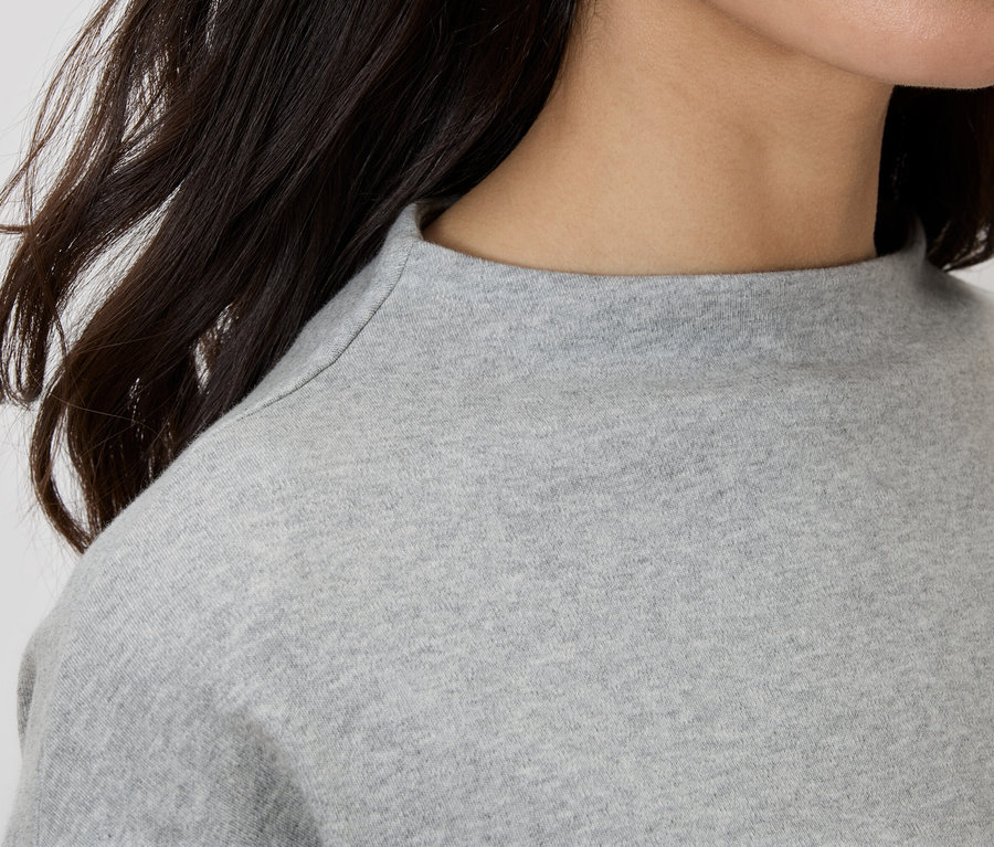 Nahaufnahme einer Frau, die ein graues Oberteil mit Rollkragen trägt.