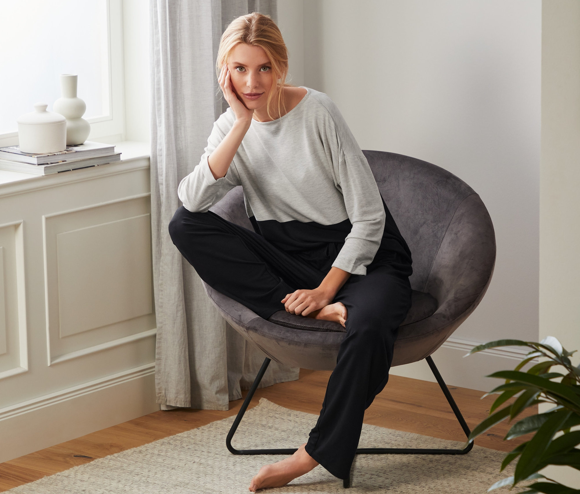 Blonde Frau sitzt in einem Sessel und trägt einen Hausanzug.