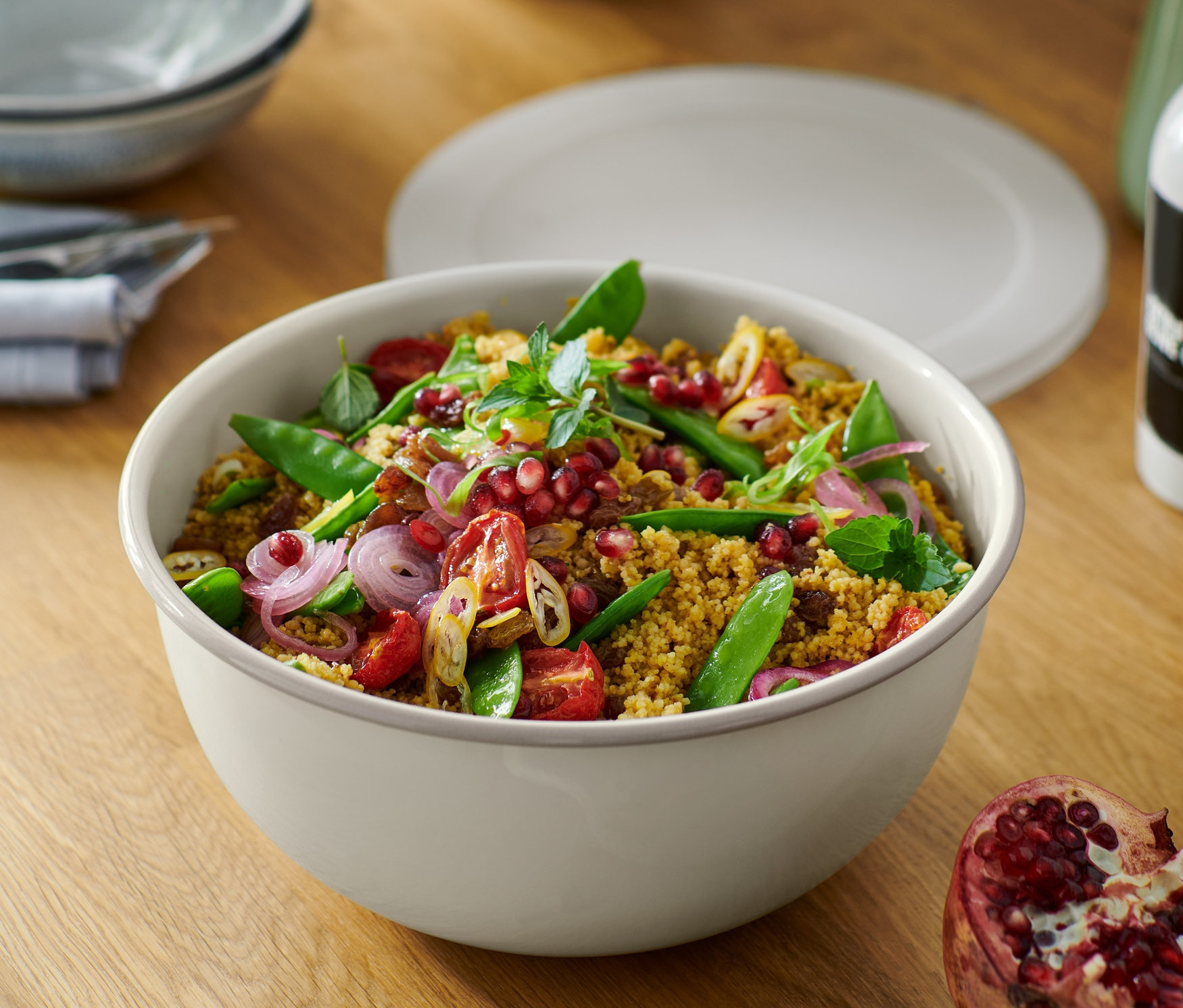 Salat in Emaille-Servier-und-Zubereitungsschüssel mit Deckel auf einem Holztisch mit Granatapfel.