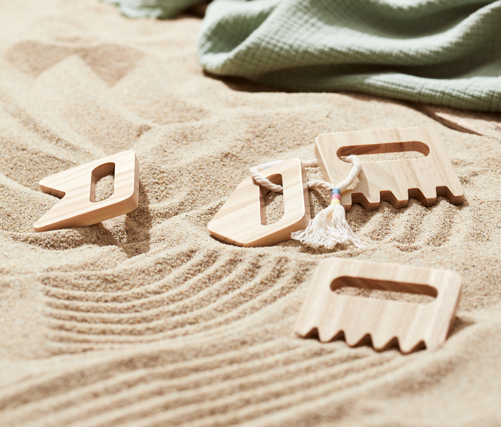 Im Sand liegen drei Kinder-Sandkämme, eine grüne Decke und Flip-Flops.