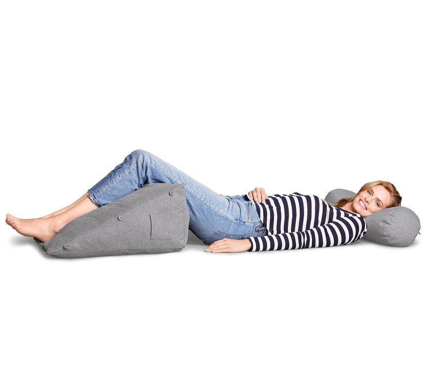 Frau liegt seitlich, die Füße auf einem grauen Rückenkissen, den Kopf auf einer Nackenrolle.