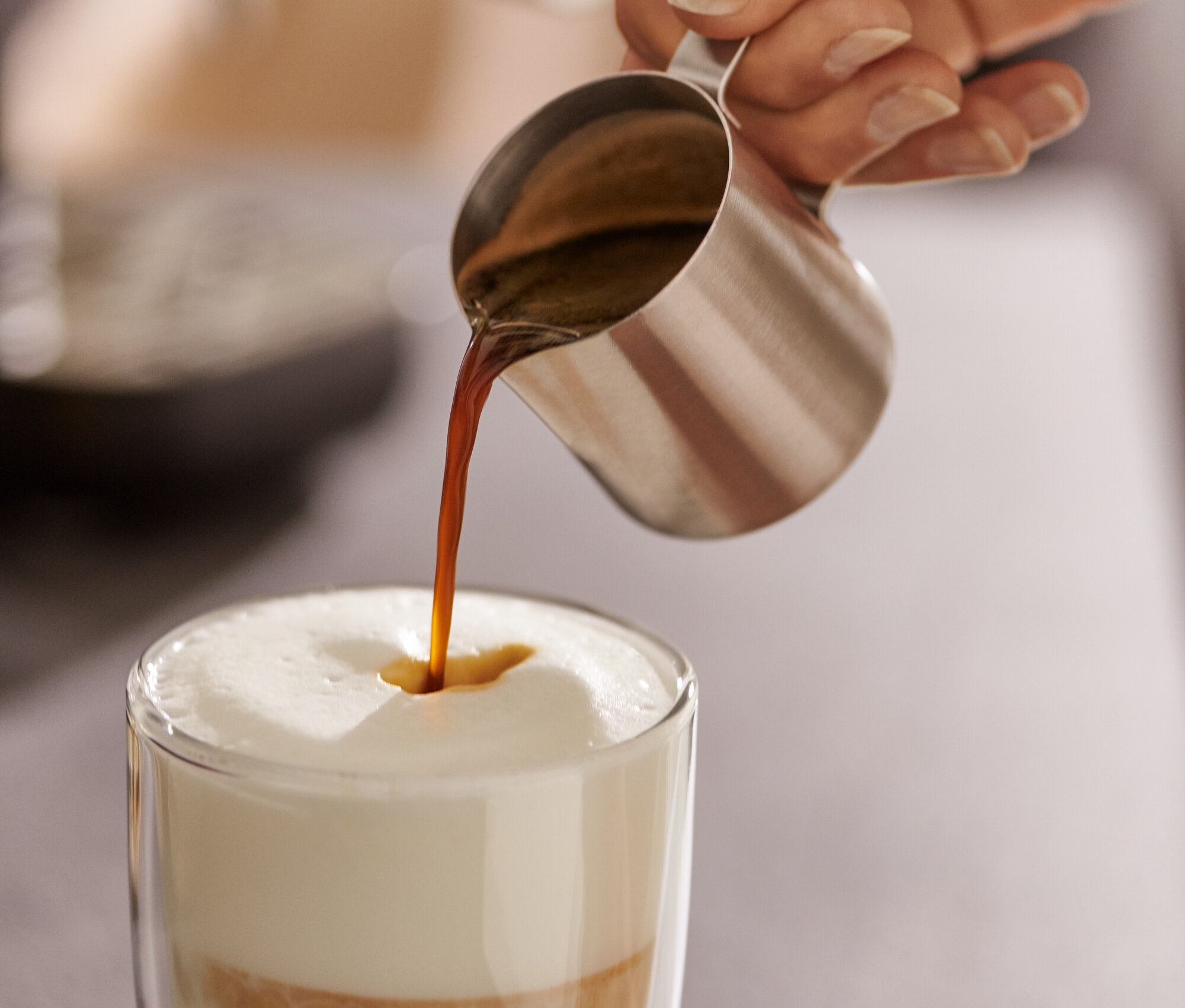 Frau gießt Espresso aus einem Espresso Kännchen, Edelstahl, 80 ml, in ein Glas Milch.