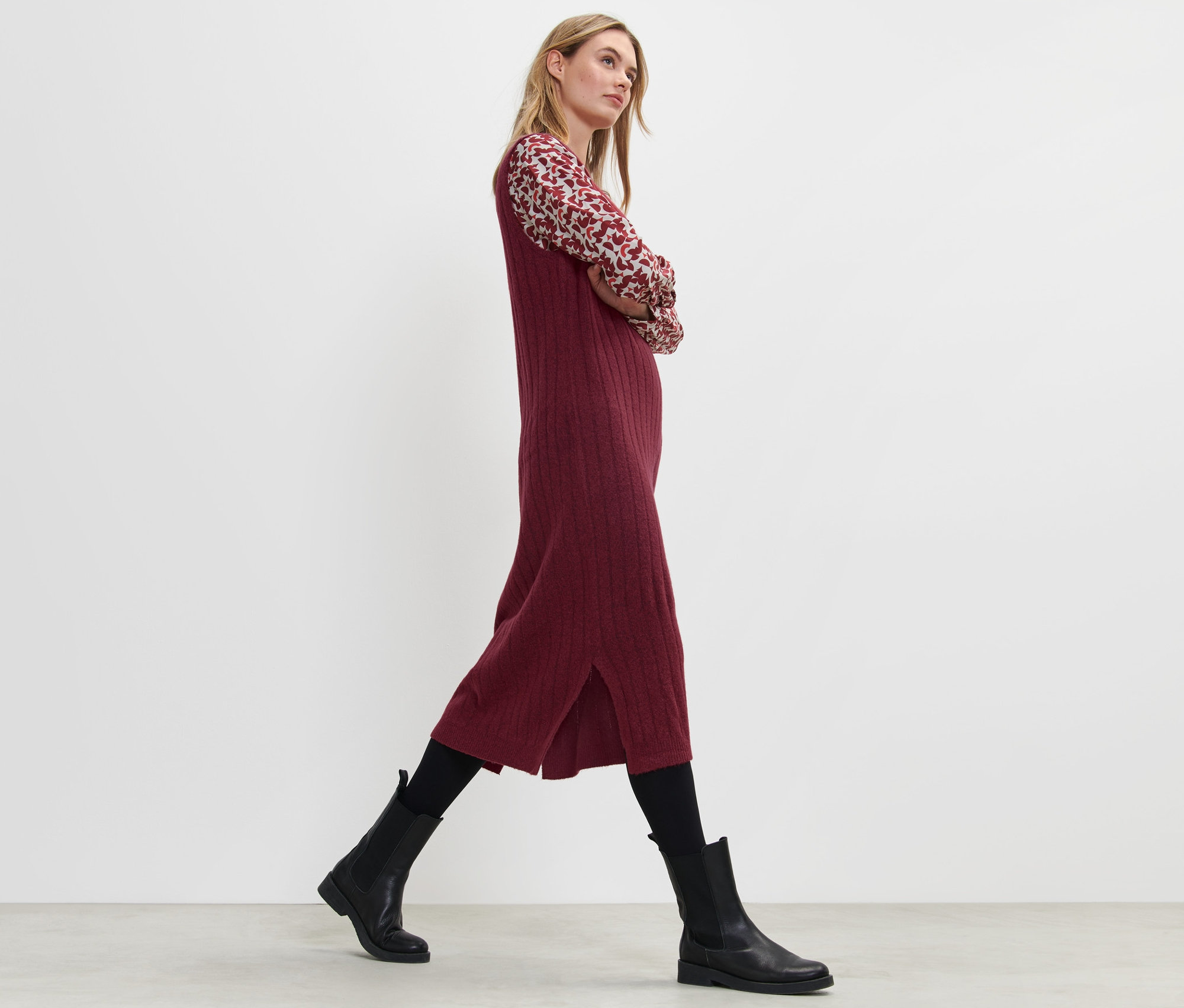 Blonde Frau geht und trägt ein geripptes Strickkleid in Rot.