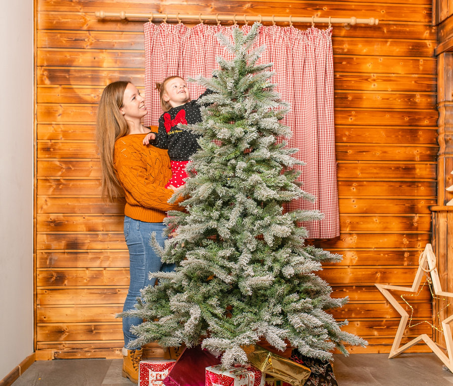 Mutter hält Tochter neben einer beschneiten Fichte Frost mit Metallständer, 180 cm.