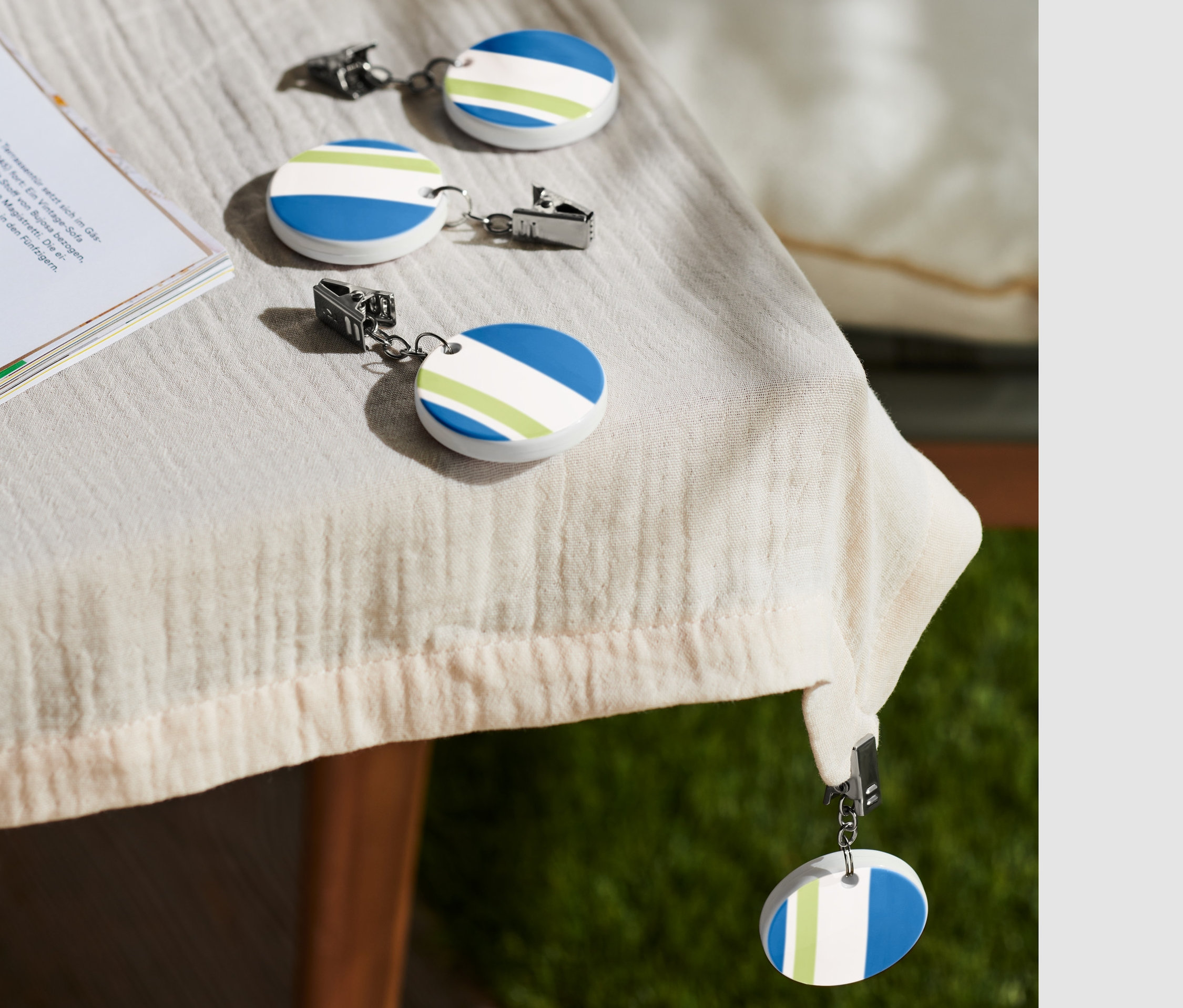 Auf einem Tisch liegen vier Tischdeckenhalter neben einer Tasse Kaffee und einem Buch.