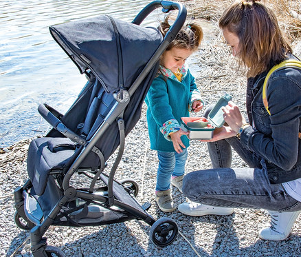Mutter öffnet Brotdose für Tochter neben Osann Sportwagen Vegas am Wasser.