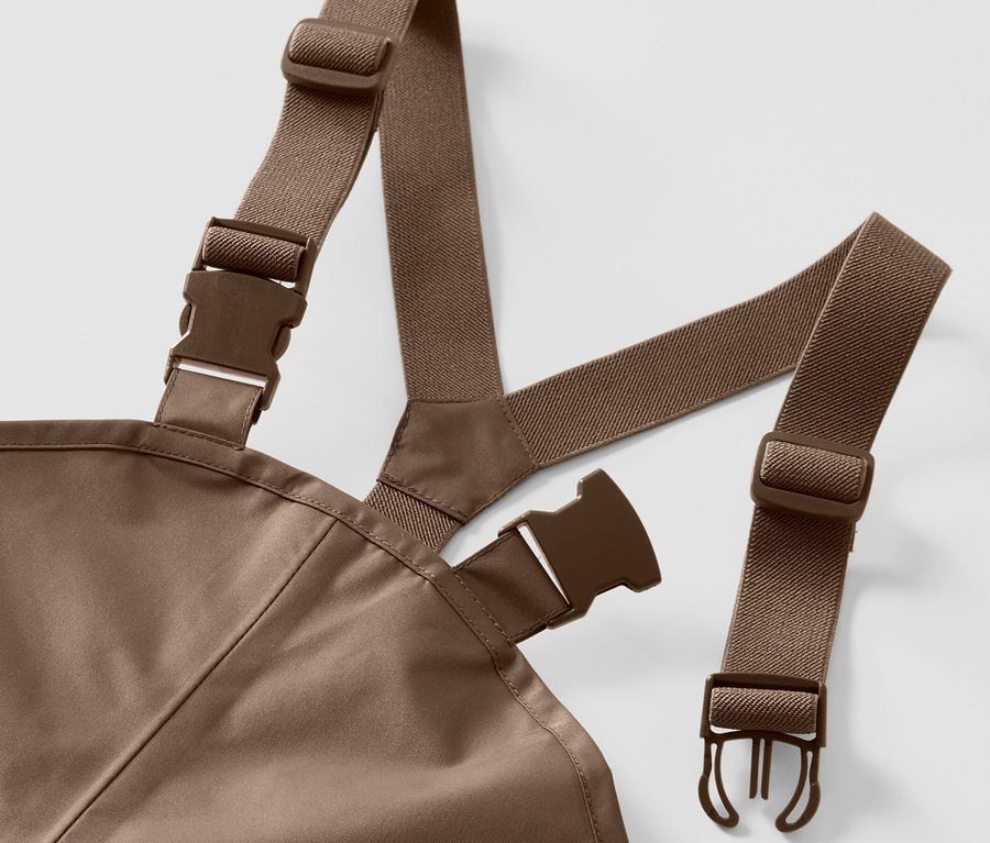 Detail einer Kinder-Regenhose mit braunen elastischen Trägern und Kunststoffschnallen auf weißem Hintergrund.