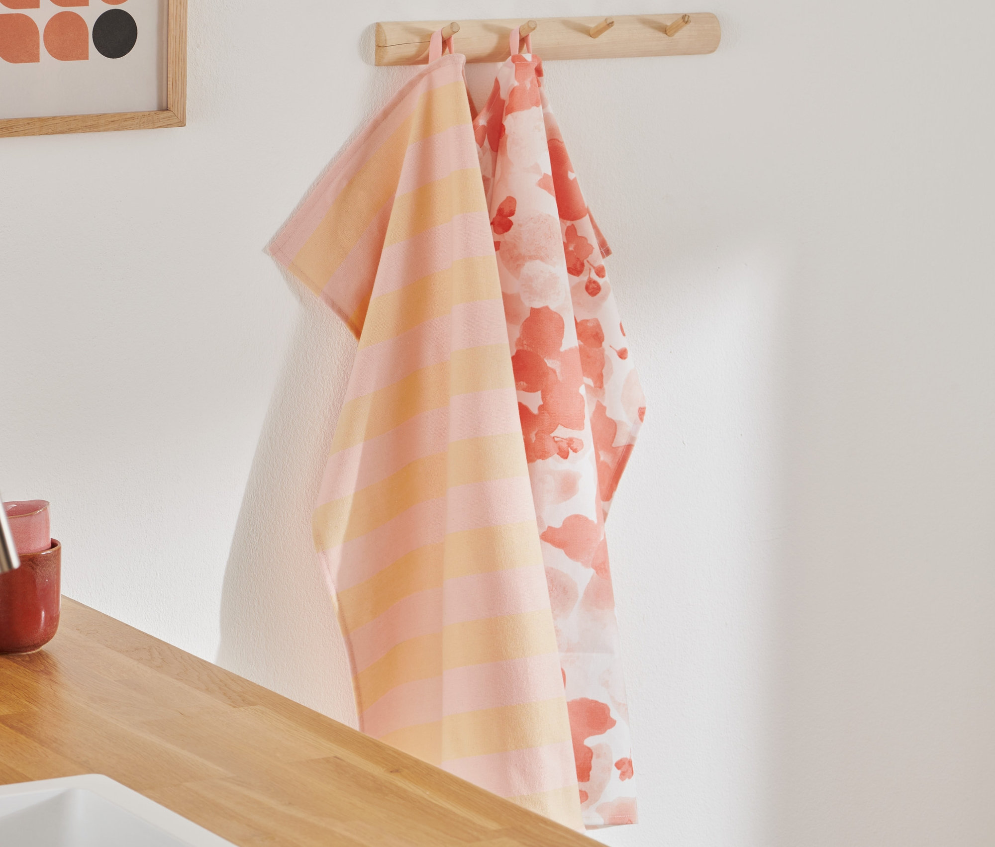 Zwei Geschirrtücher hängen an einem Haken. Eines ist orange-rosa gestreift, das andere hat ein Blumenmuster.