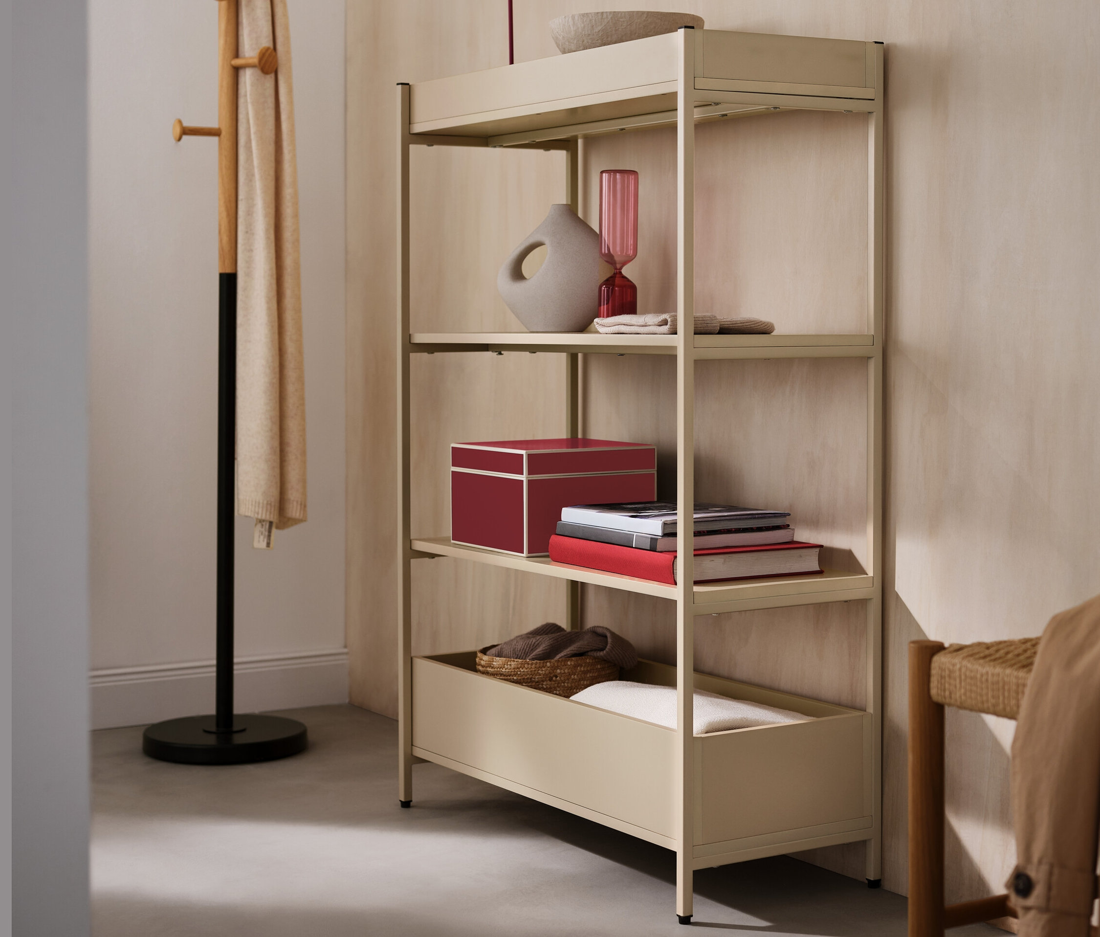 Ein beiger Konsolentisch mit vier Regalen, auf dem sich eine rote LED-Akku-Tischleuchte, eine Vase und eine Schale befinden. Daneben steht ein Garderobenständer.