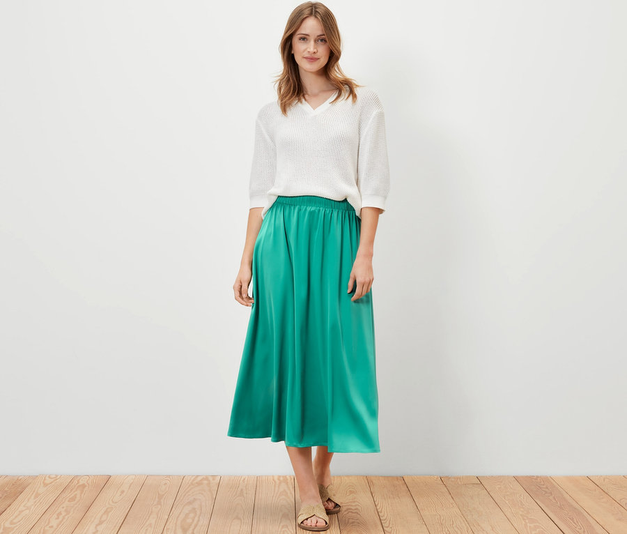 Frau posiert in weißem Oberteil und grünem Satinrock.