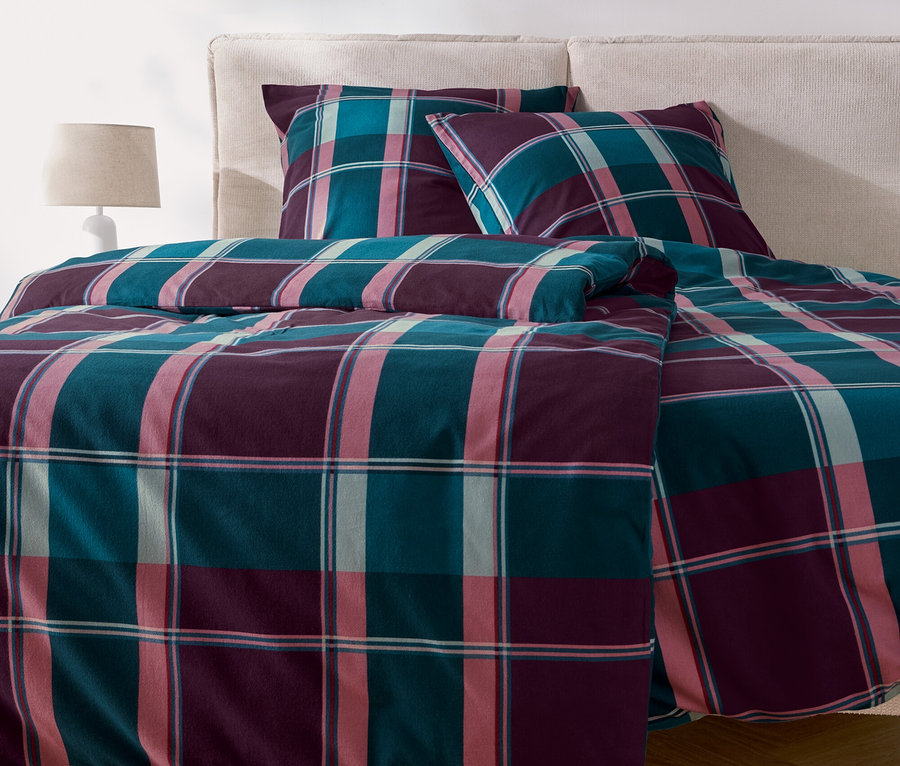 Ein kariertes Bettzeug mit Kissen liegt auf einem Bett.