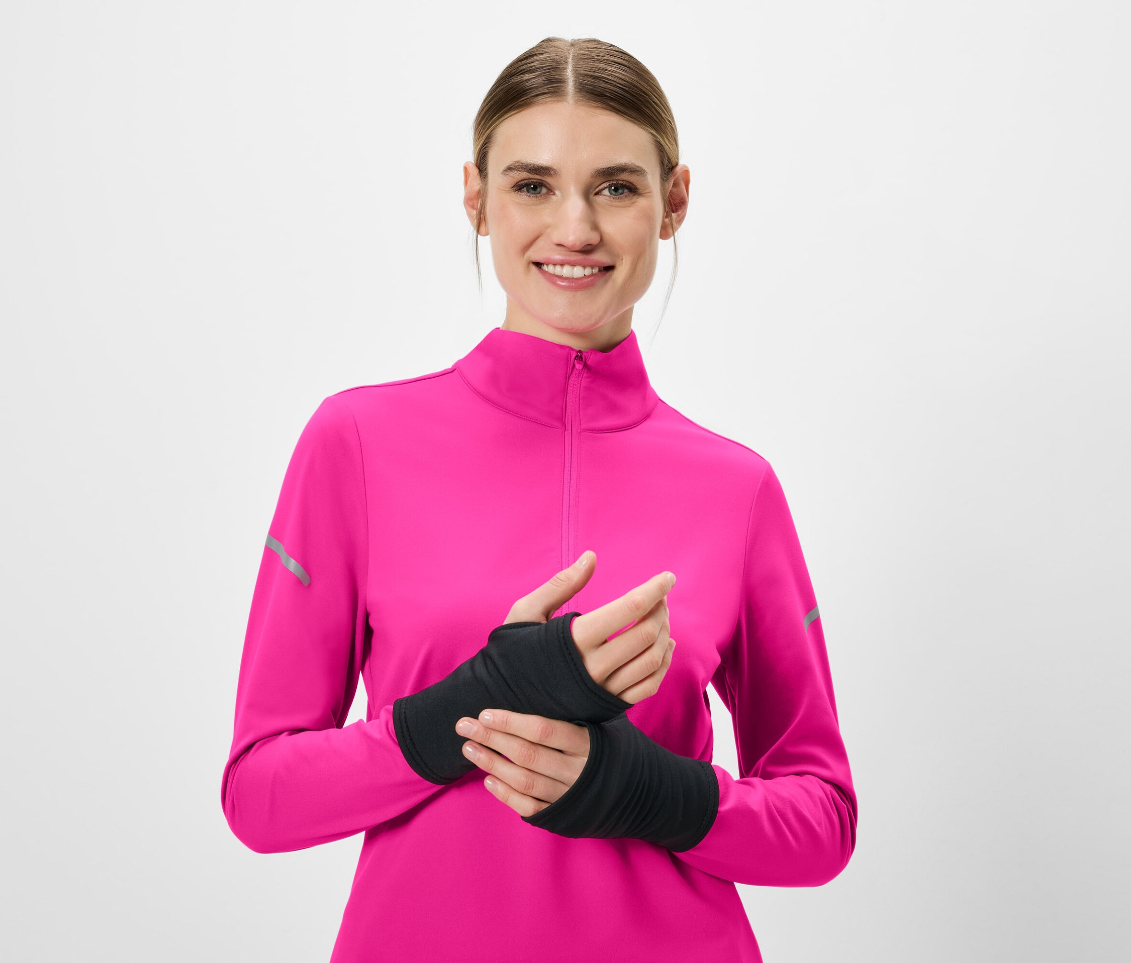 Lächelnde Frau trägt ein pinkfarbenes Langarmshirt und schwarze Armstulpen.