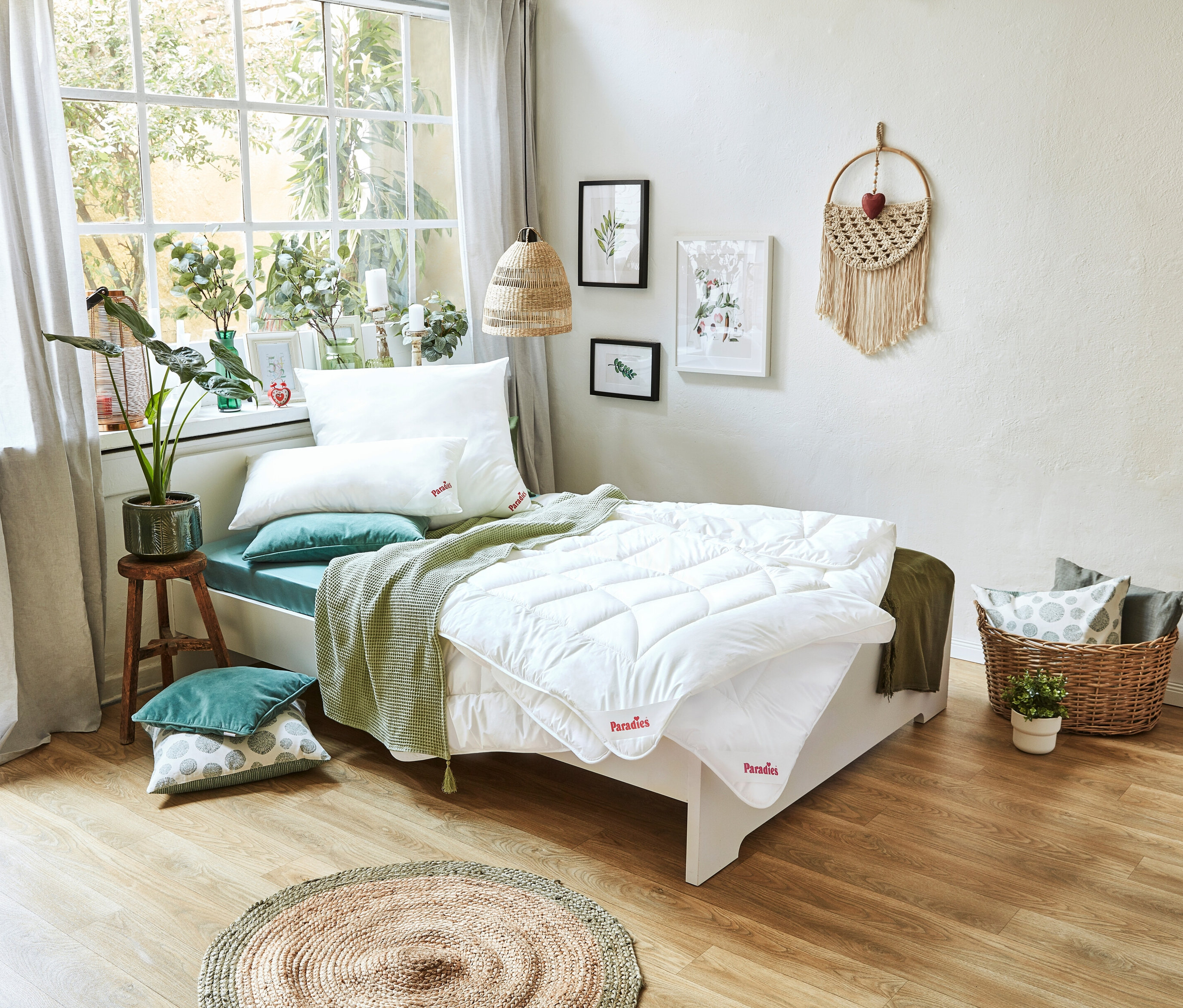 Zimmer mit Bett mit weißer Decke und Kissen, neben dem Bett steht ein Tisch mit einer Topfpflanze.