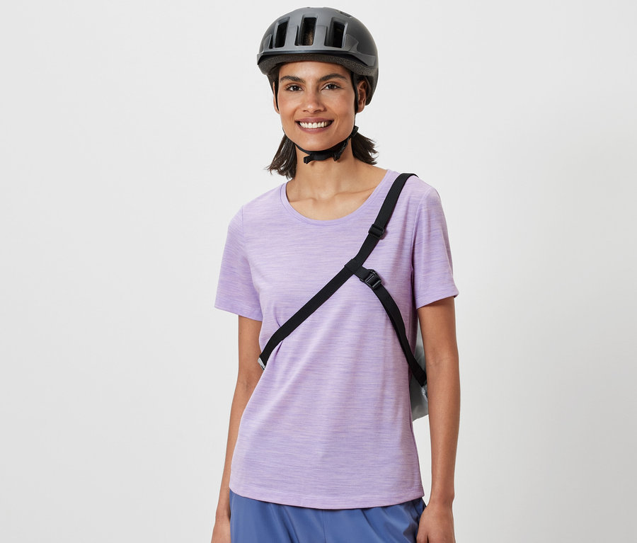 Lächelnde Frau mit Fahrradhelm und Fahrrad-Einkaufstasche über der Schulter.