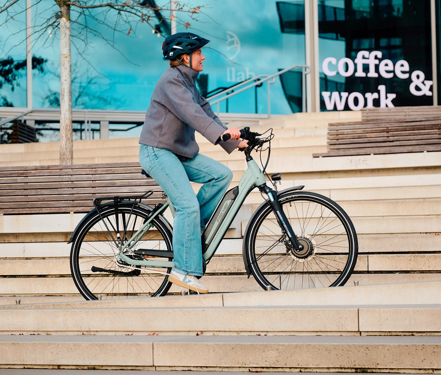 Frau fährt ein Fischer City E-Bike CITA 2403 ACTIVE, entweder 50 cm oder 43 cm, eine Treppe hinunter.