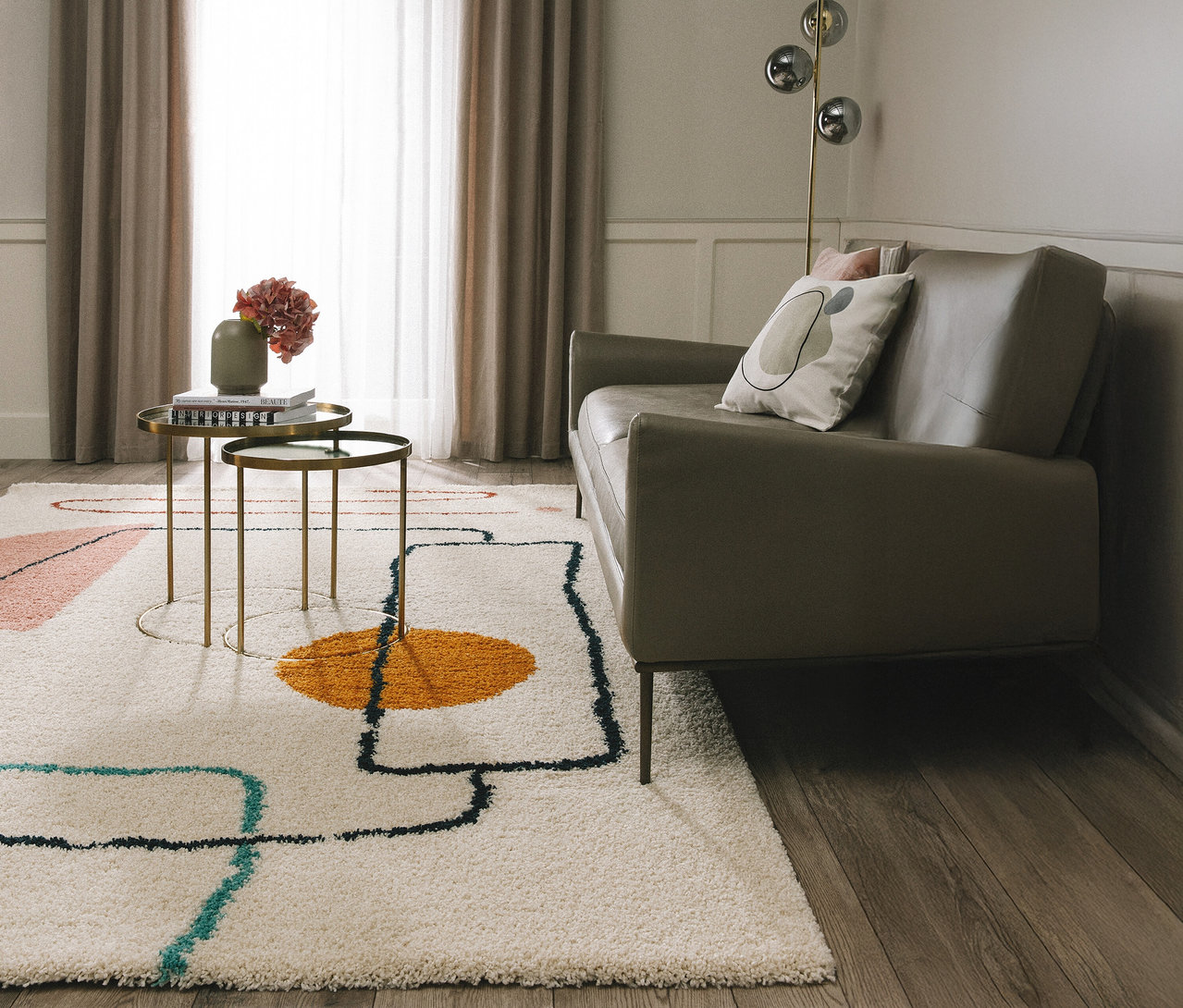 Wohnzimmer mit beigem Sofa, Couchtisch mit Blumen und abstraktem Teppich.