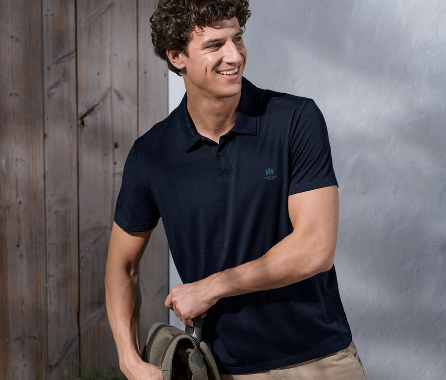 Mann mit Rucksack trägt ein Funktionspoloshirt mit Merinowolle und beigefarbene Shorts.