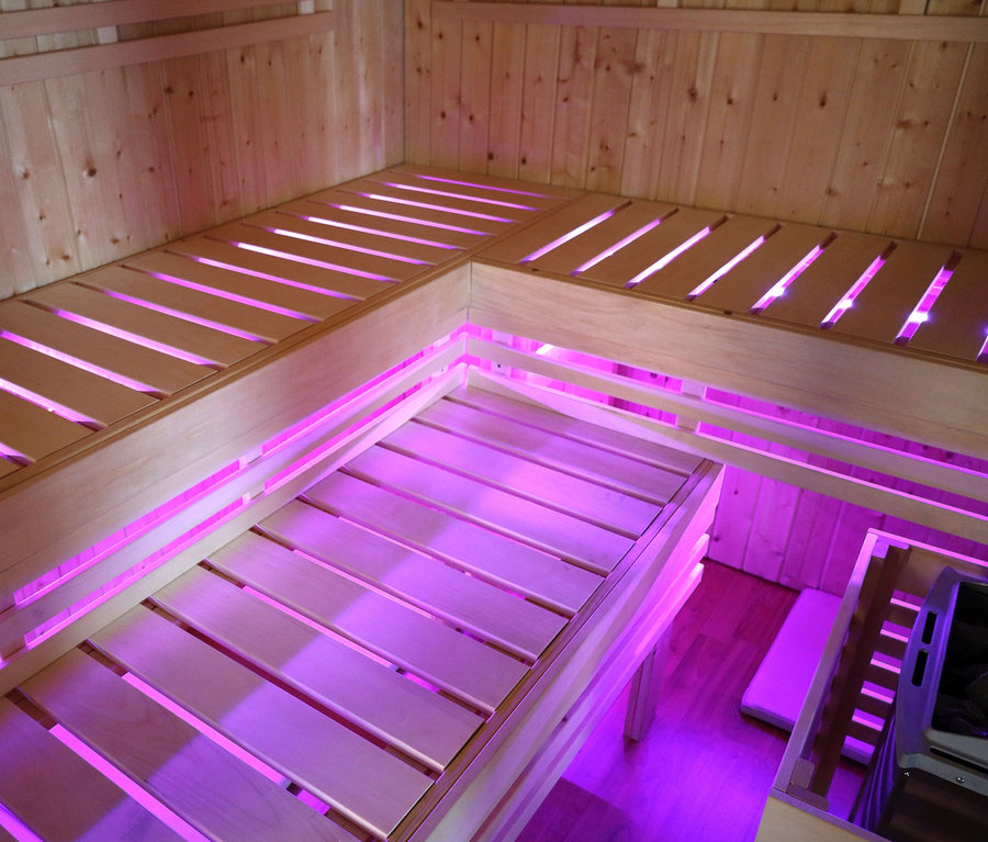 Innenansicht einer Karibu Fasssauna »Nadi 3« mit Holzbänken und violetter Beleuchtung.