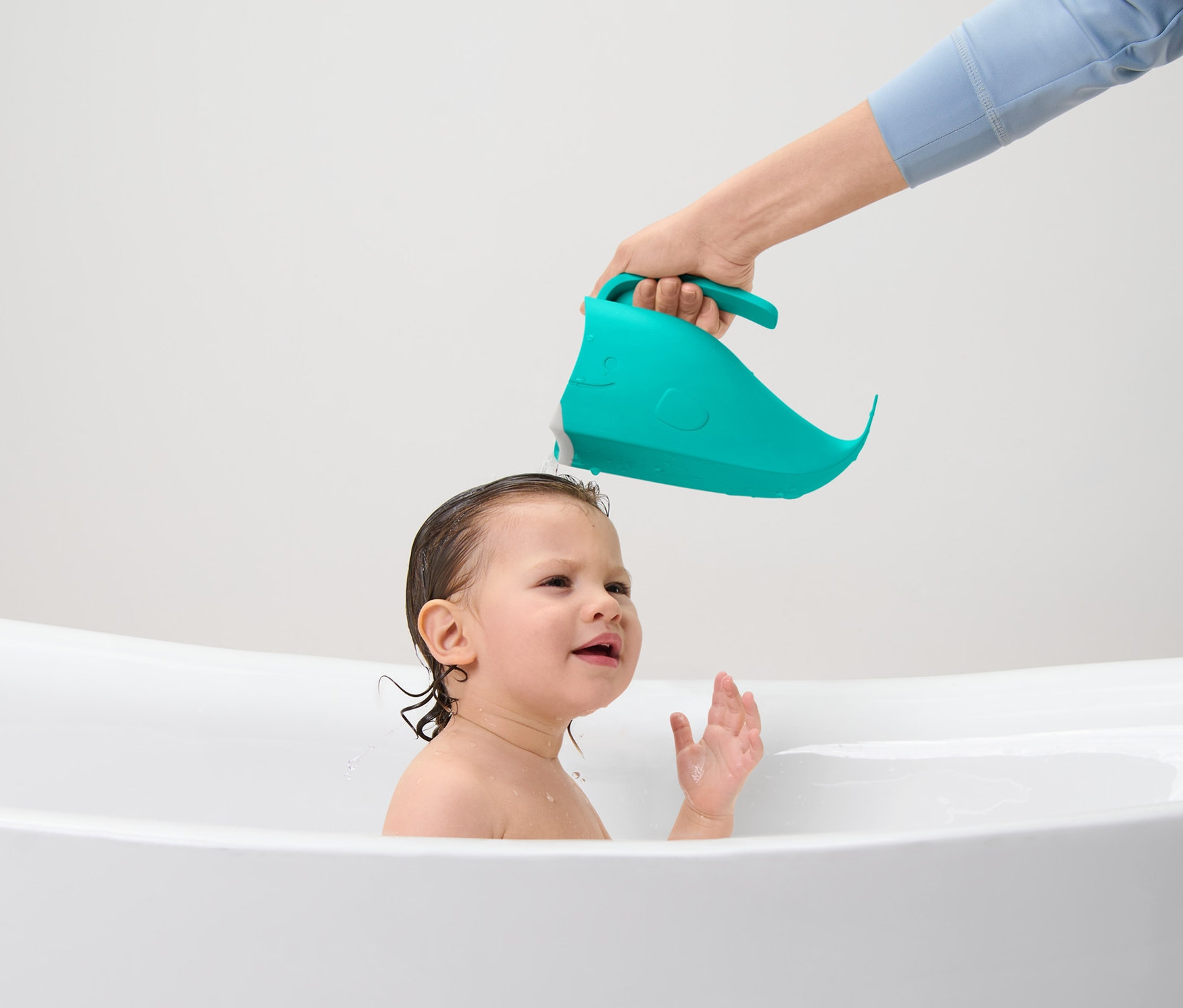 Ein Elternteil wäscht die Haare eines Kindes mit einem Kinder-Haarwaschbecher in einer Badewanne.
