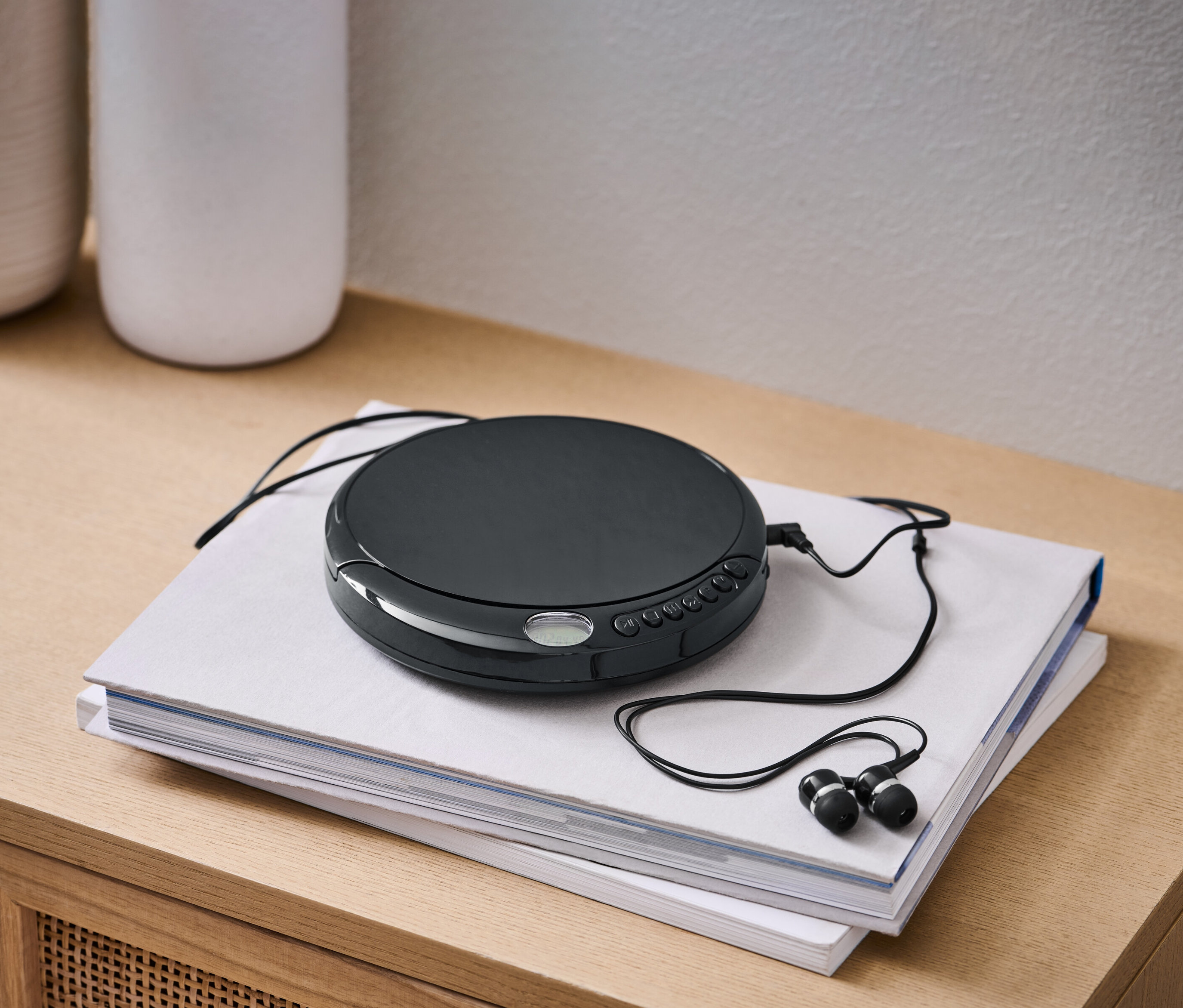 Ein schwarzer, tragbarer CD-Player mit schwarzen Kopfhörern liegt auf zwei Büchern.
