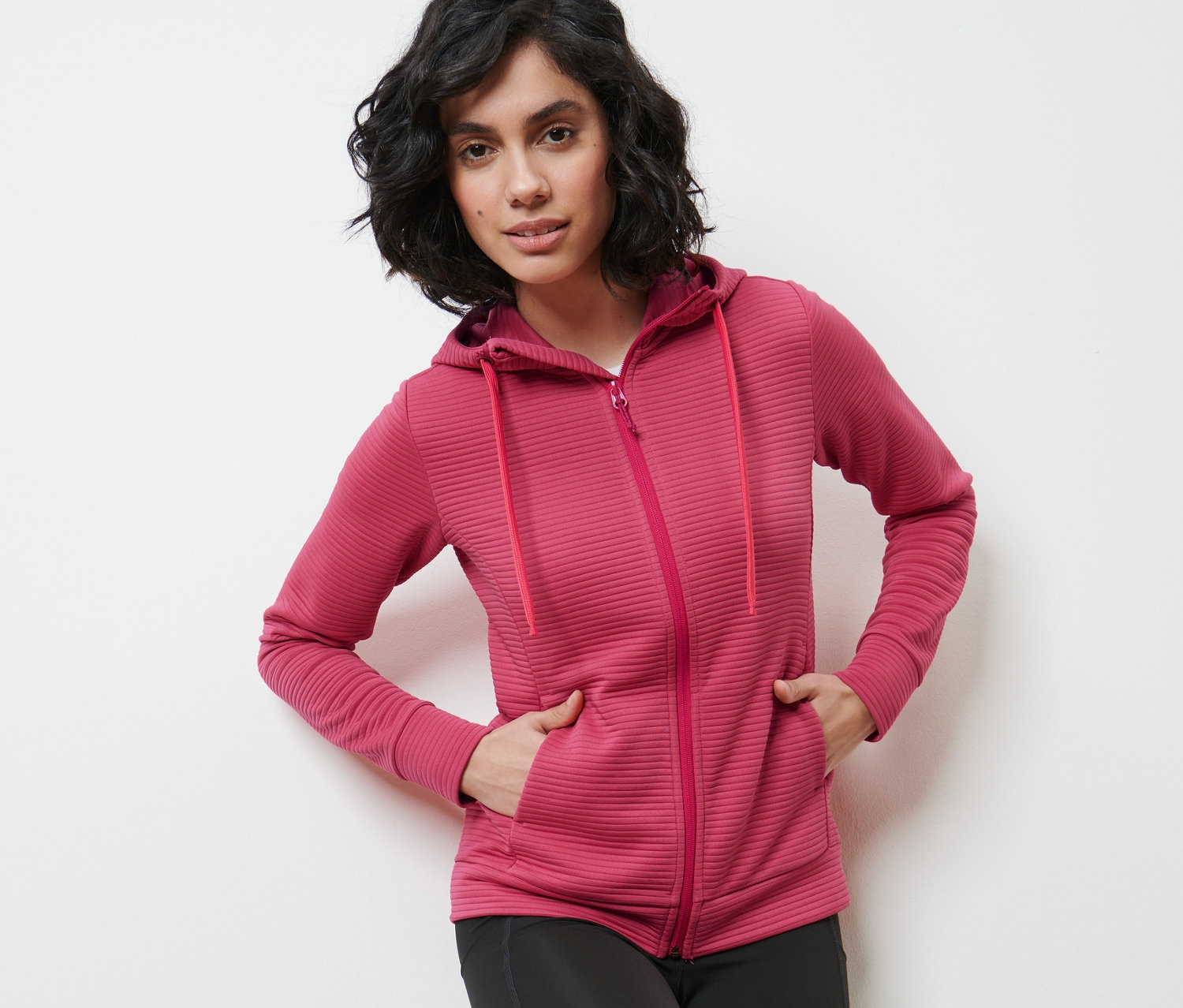 Frau posiert in beerefarbener Kapuzenjacke und schwarzen Leggings.