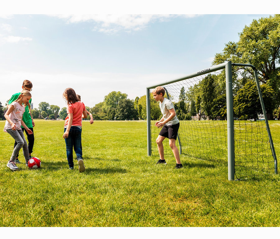 Vier Kinder spielen Fußball auf einer Wiese in der Nähe eines HUDORA Fußballtors »Expert 240«.