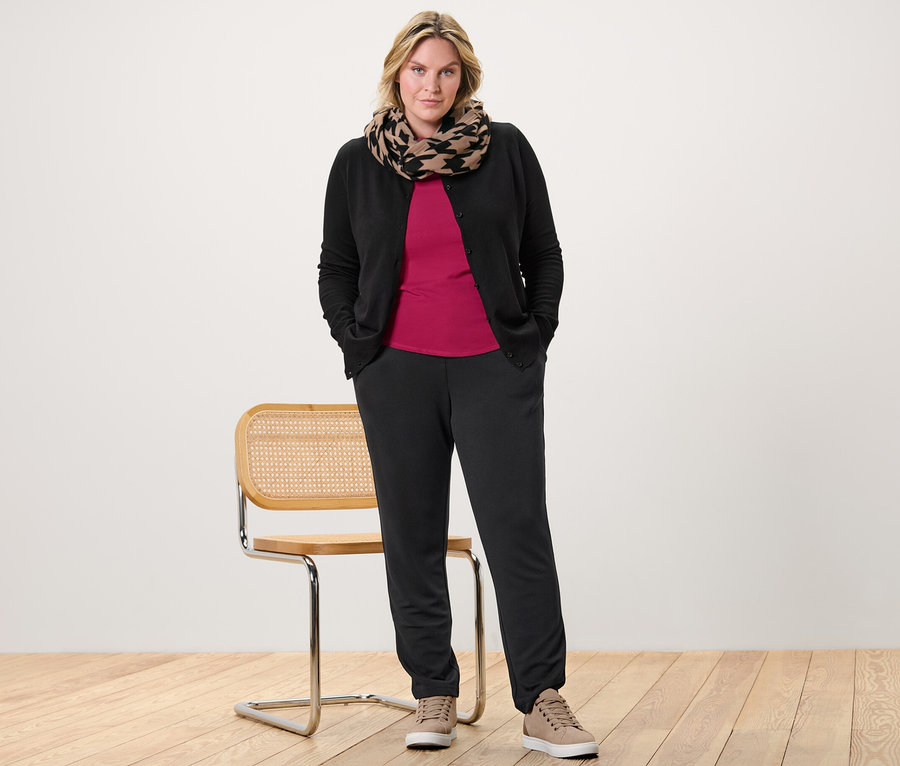 Frau posiert mit einem himbeerroten Shirt mit 3/4-Arm, einem Feinstrick-Cardigan und einer Joggpants.