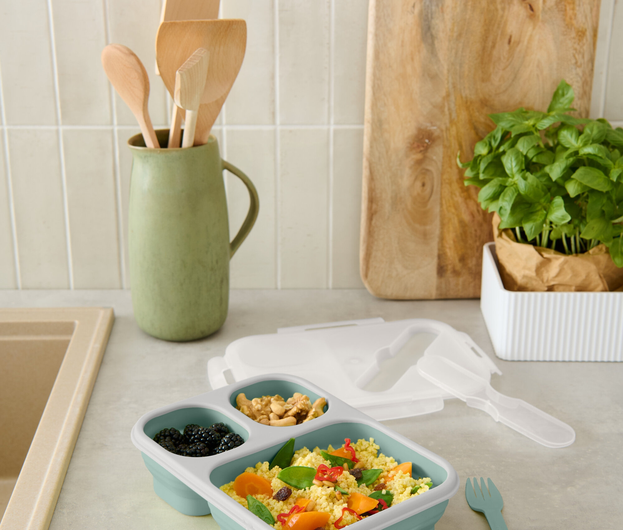 Eine blaue, unterteilte Lunchbox mit Brombeeren, Nüssen und Couscous mit Gemüse steht auf der Theke.