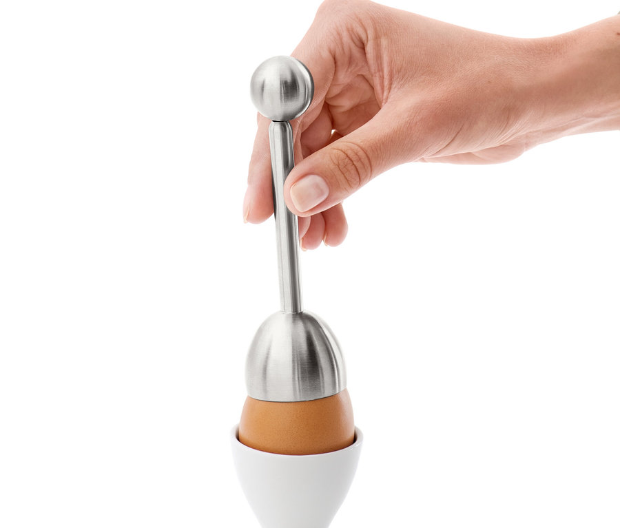 Eine Hand verwendet einen Eierköpfer auf einem Ei in einem weißen Eierbecher.