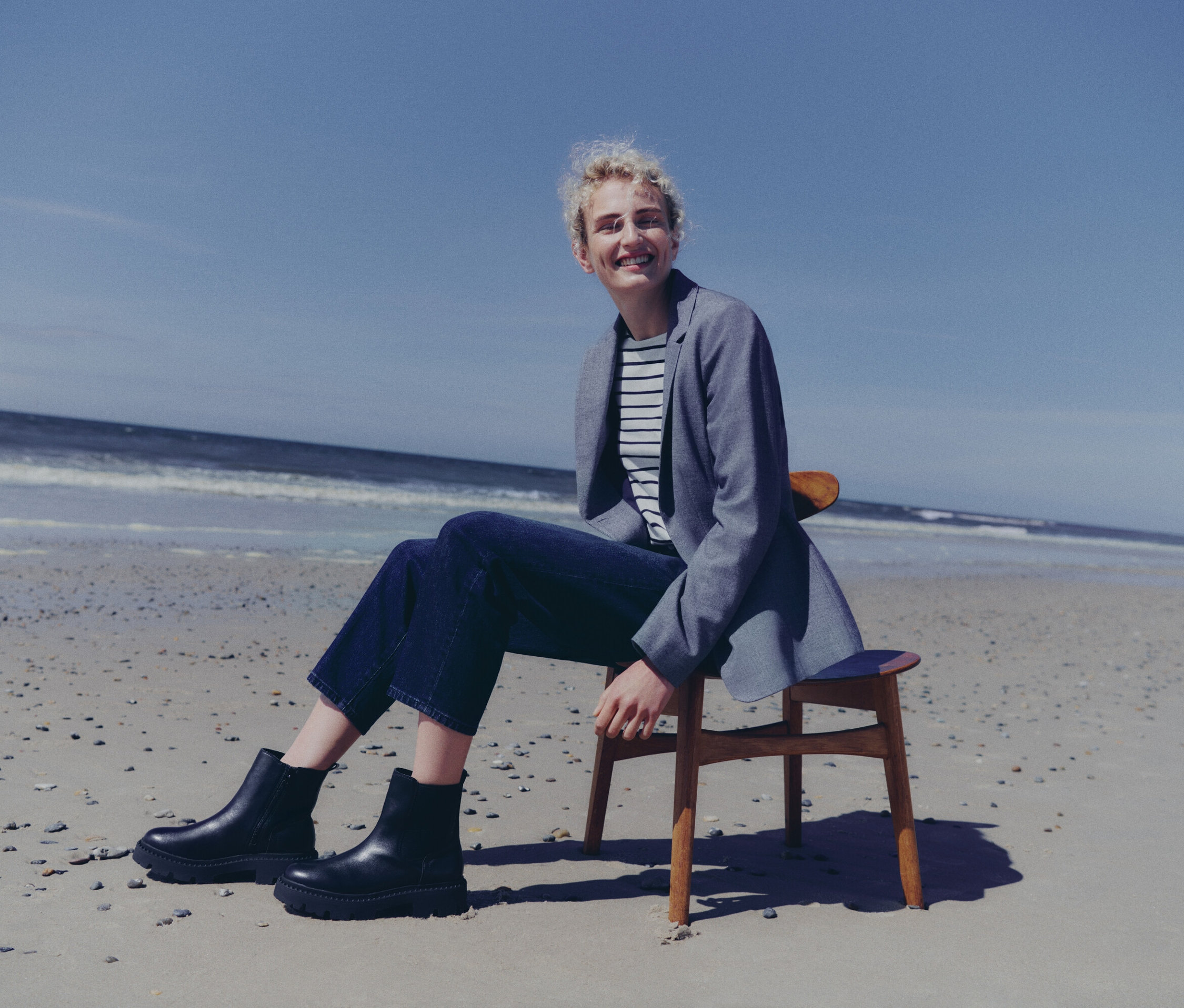 Eine Frau sitzt am Strand auf einem Stuhl und trägt schwarze Tom Tailor Stiefeletten mit breiter Sohle.