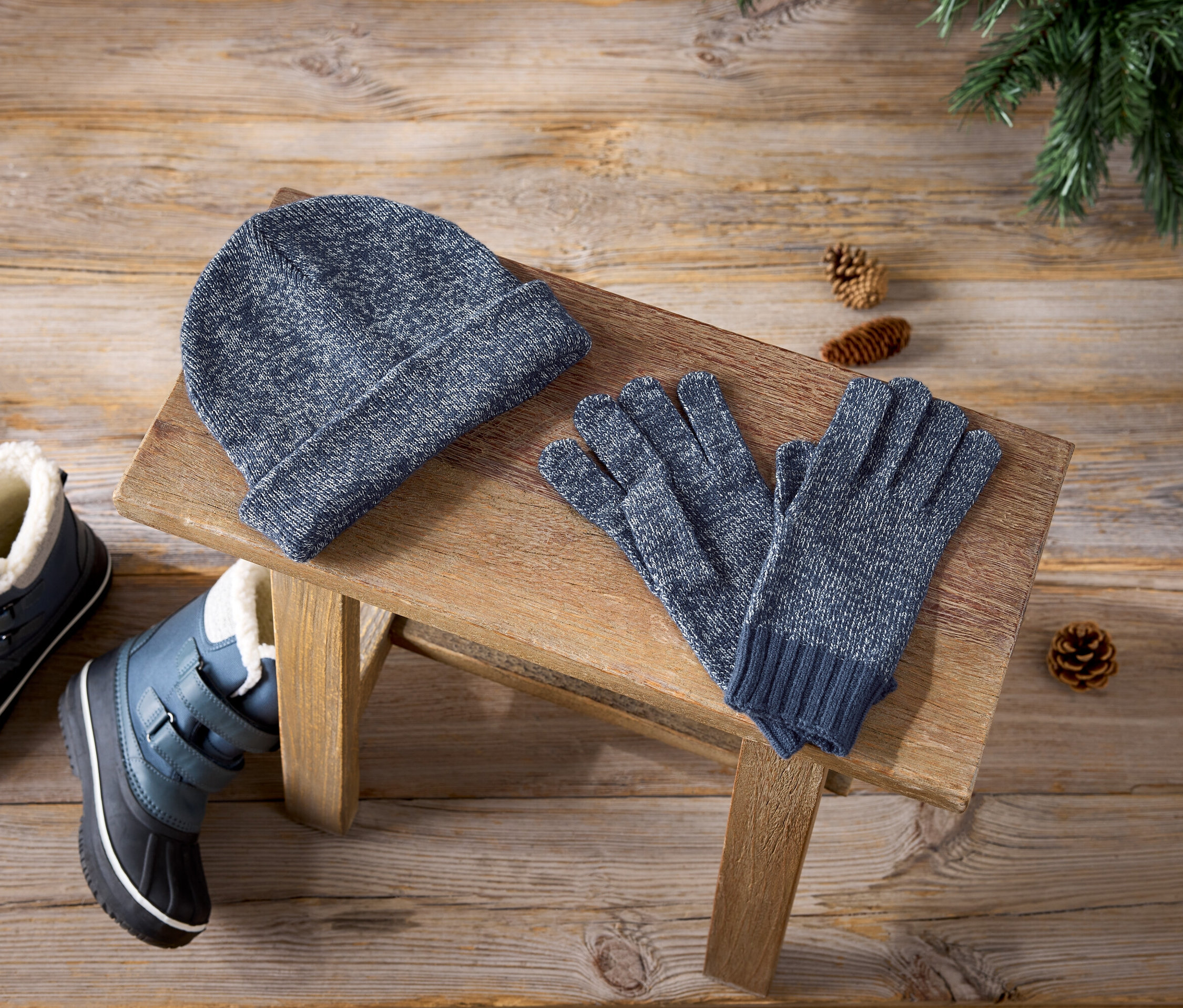 Blaue Mütze, Handschuhe und Winterstiefel auf einem Holzhocker.