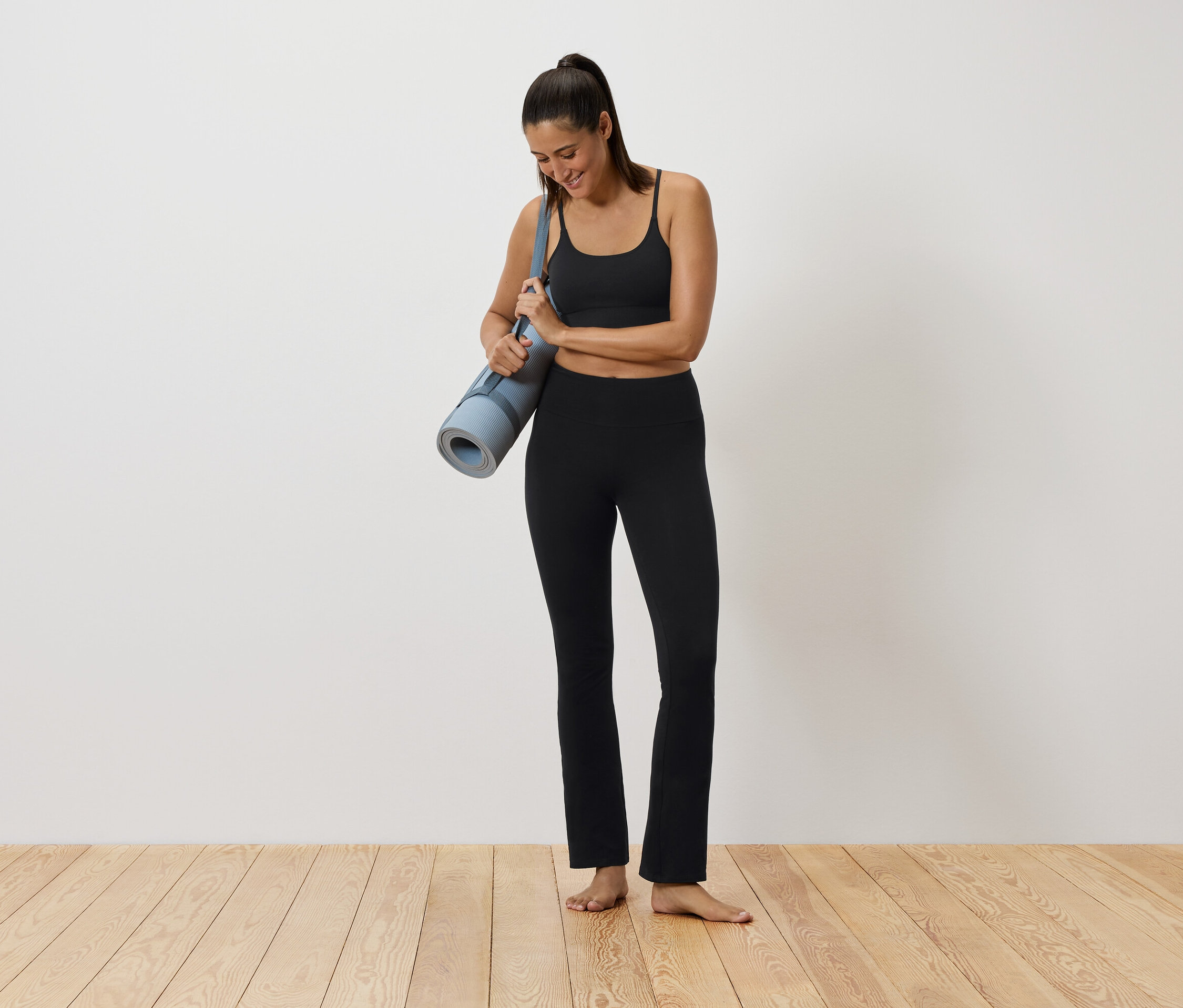 Frau in schwarzer Sportbekleidung hält eine Yogamatte.