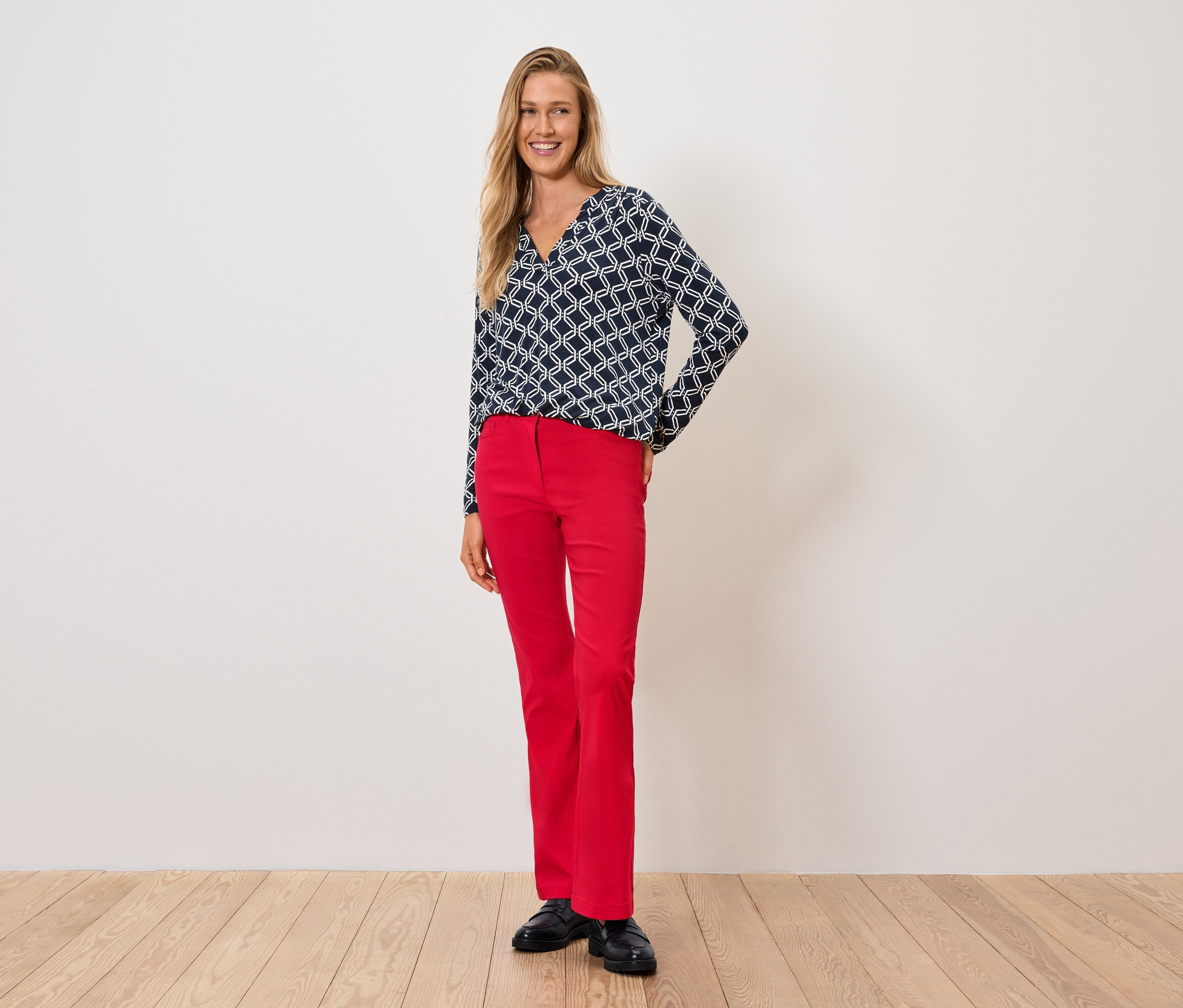 Frau in blau-weißem Oberteil und roter Hose steht auf Holzboden.