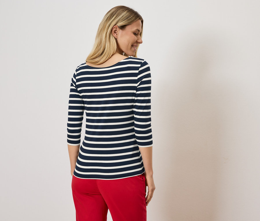 Blonde Frau trägt ein blau-weiß gestreiftes Shirt und rote Hosen.