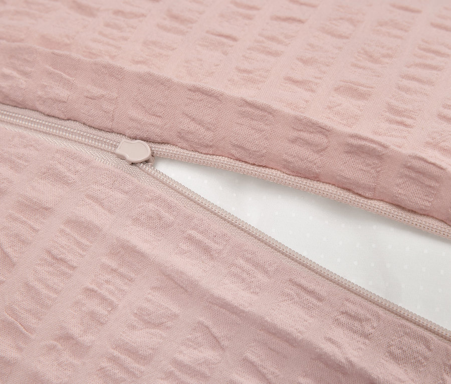 Detailaufnahme eines rosafarbenen Bettbezugs mit Textur und einem Reißverschluss, der das weiße Innere teilweise enthüllt.