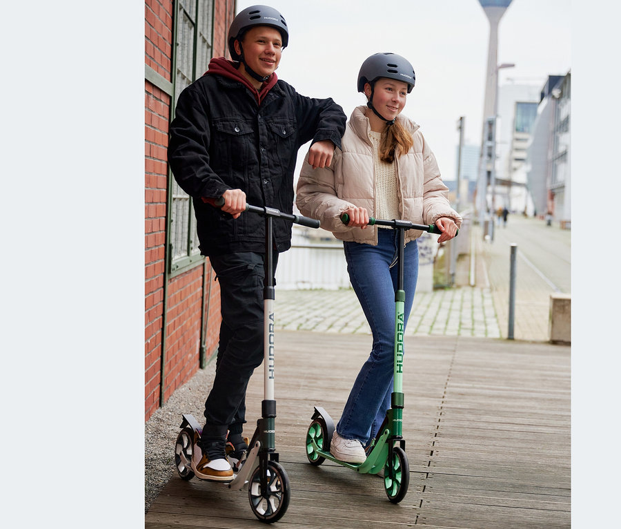 Zwei Kinder mit Helmen stehen draußen auf HUDORA BigWheel® 205 advanced Scootern, einer grün, einer grau-weiß.