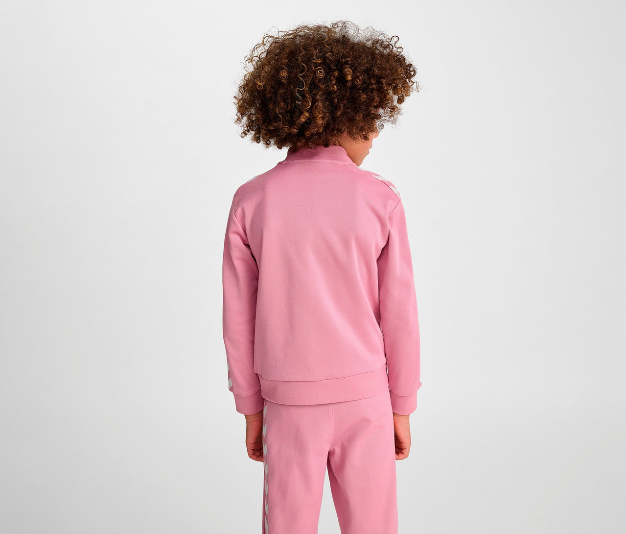 Mädchen mit dem Rücken zur Kamera trägt einen rosa HUMMEL HMLJR Archive Reg Poly Zip Jacket Trainingsanzug.