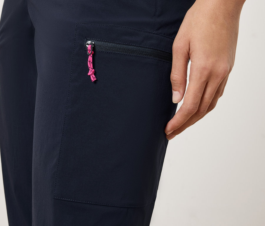 Nahaufnahme einer Person, die eine marineblaue Hose mit einer Reißverschlusstasche und einem pinkfarbenen Kordelzug trägt.