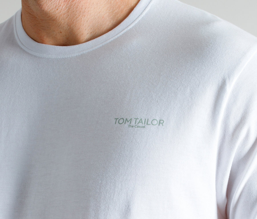 Nahaufnahme von Hals und Schultern eines Mannes, der ein weißes T-Shirt mit dem Aufdruck TOM TAILOR The Casual trägt.