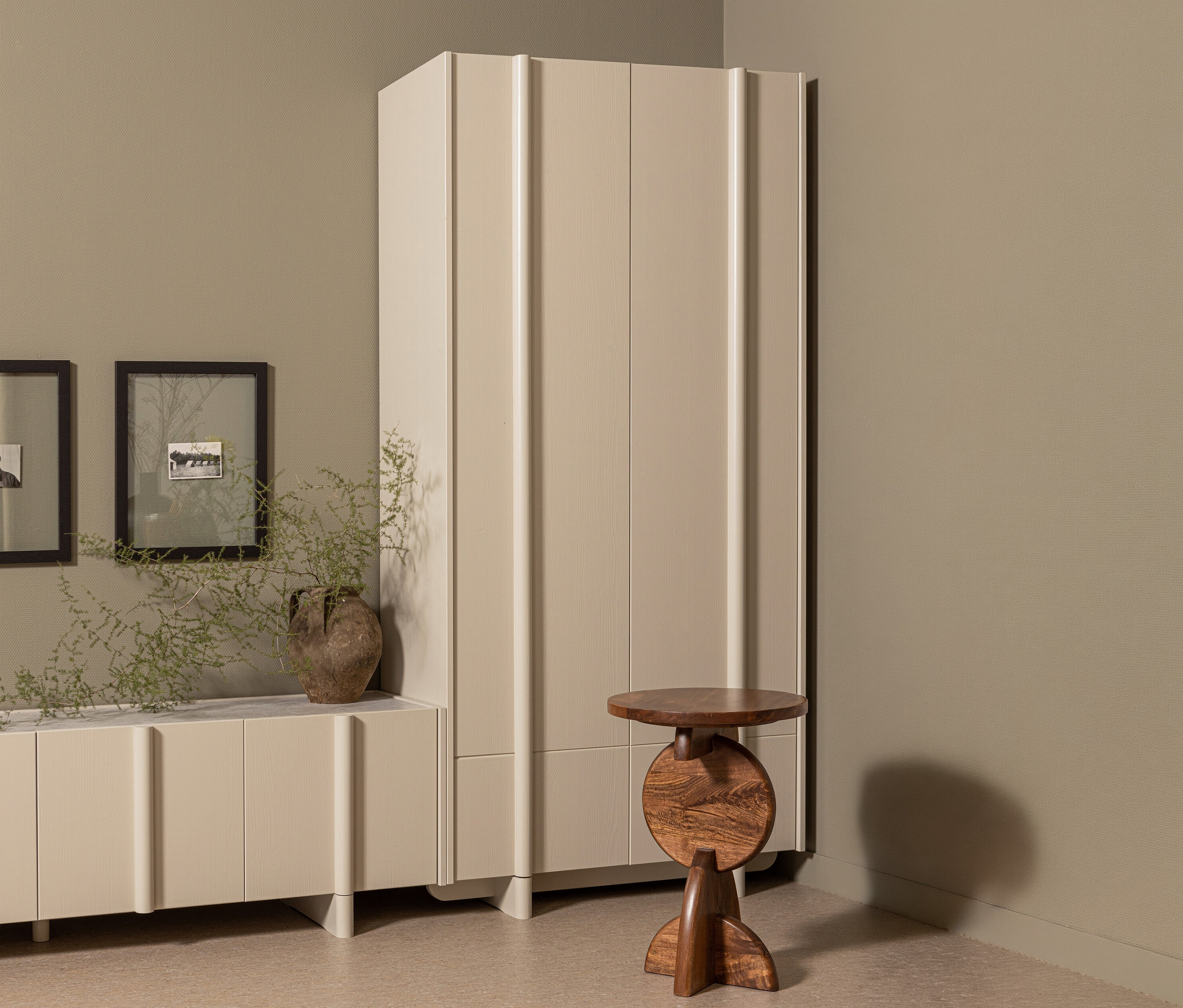 Ein WOOOD Lagerschrank »Basu« kiefer dust steht neben einem braunen Holztisch in einem Raum mit einem Sideboard und zwei gerahmten Bildern.