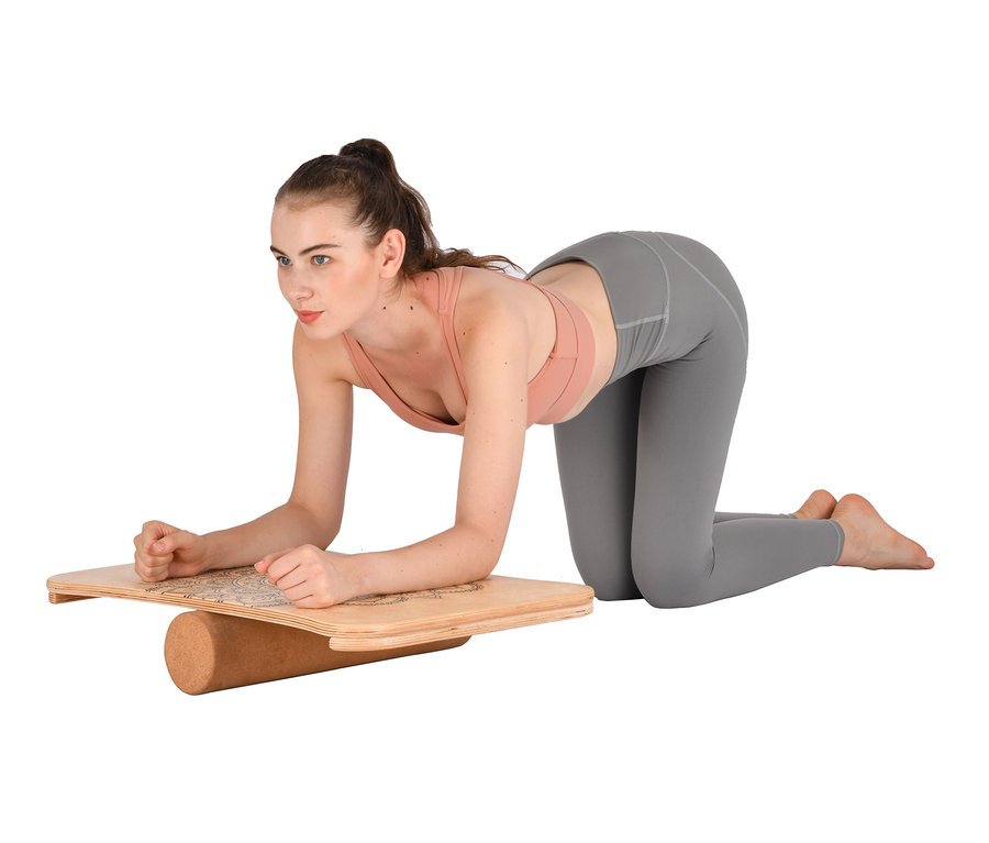 Frau in rosafarbenem Sport-BH und grauen Leggings kniet auf einem Balance-Board.