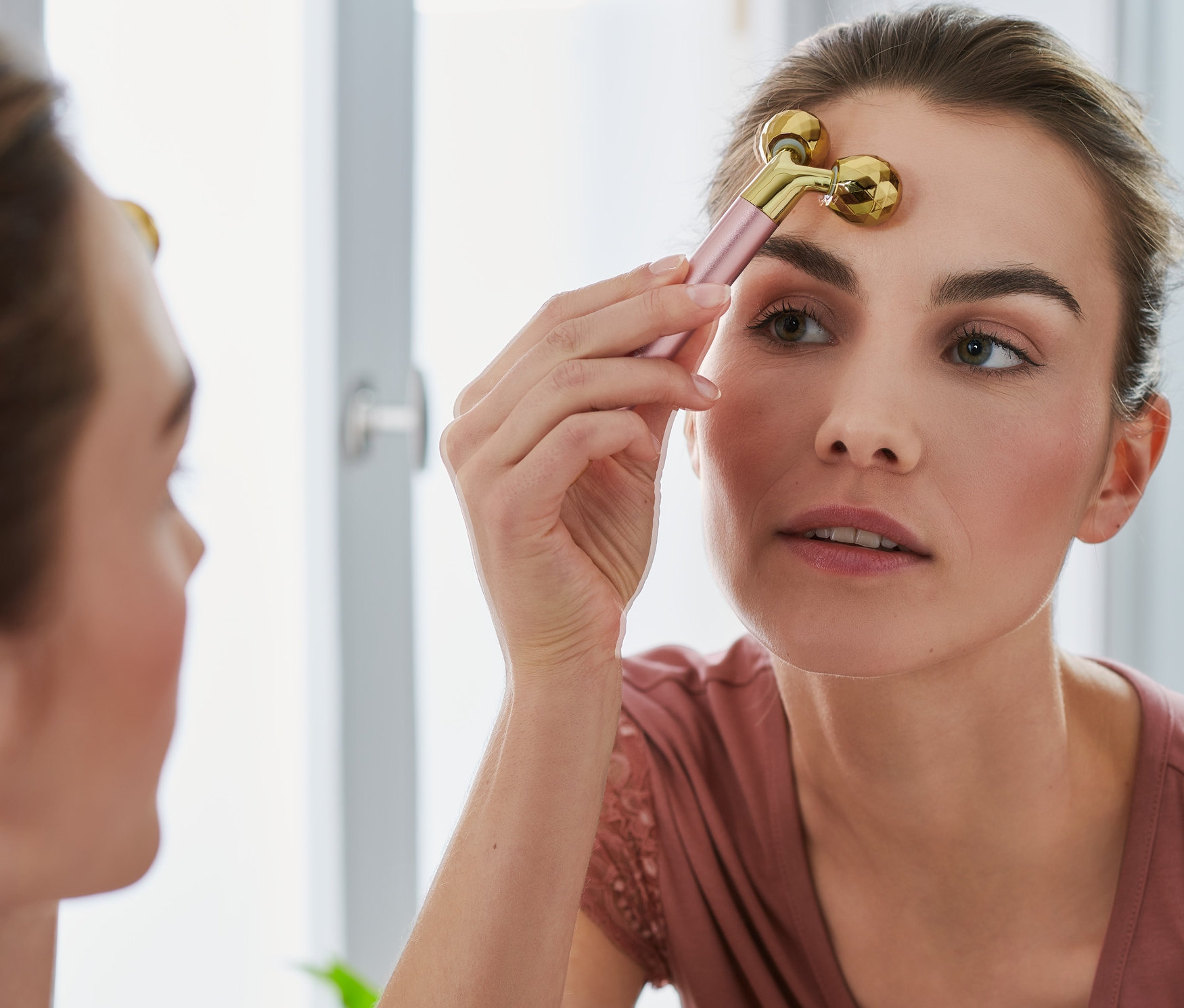 Frau verwendet 2-teiliges Gesichtsmassage-Set auf ihrer Stirn vor einem Spiegel.