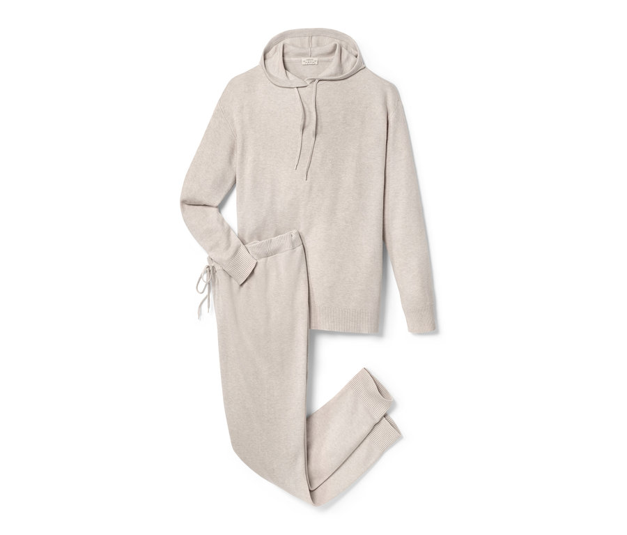 Eine beige Umstands-Loungekombination aus Kapuzenpullover und Hose liegt auf einem weißen Hintergrund.