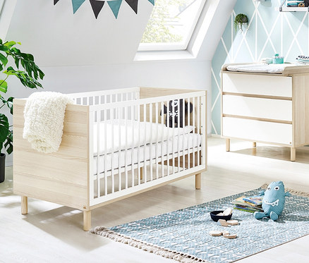 Ein Kinderzimmer mit Pinolino Babybett »Flow«, Kommode und blauem Teppich.